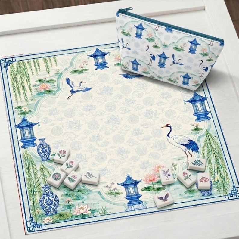 May include: A square fabric mat and a matching zippered pouch featuring a blue and white print of cranes, lotus flowers, willow trees, and pagodas. Several white rectangular mahjong tiles with colourful floral and bird motifs are scattered on the mat.