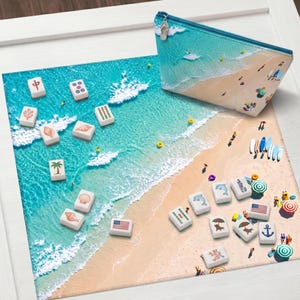 Può includere: Una pochette rettangolare con cerniera e un tappetino quadrato con una scena di spiaggia con acqua turchese e sabbia. Sulla superficie sono sparse tessere bianche da mahjong decorate con vari simboli, tra cui palme, conchiglie e delfini.