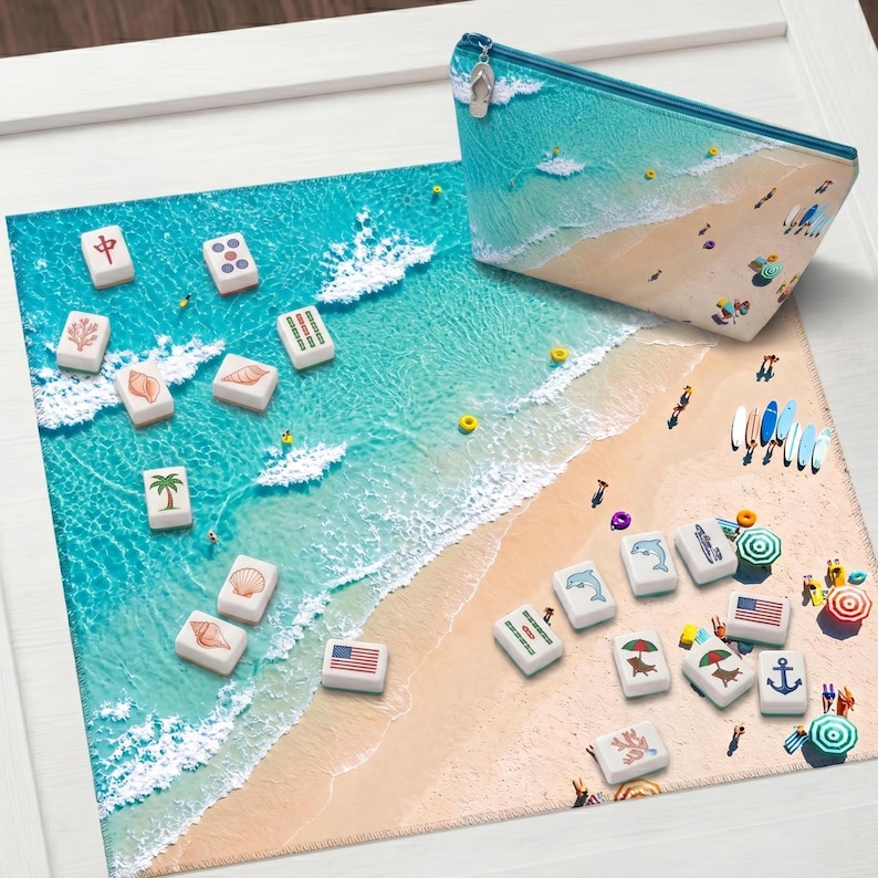 May include: A rectangular zippered pouch and a square mat featuring a beach scene with turquoise water and sand. Scattered across the surface are white mahjong tiles decorated with various symbols, including palm trees, shells, flags, and dolphins.