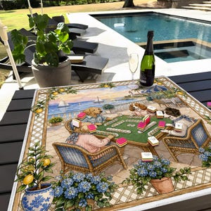 May include: A decorative square table mat featuring a whimsical illustration of dogs playing mahjong on a patio overlooking the ocean. The mat has a border with lemons and flowers, with a bottle of champagne and a glass on the table.