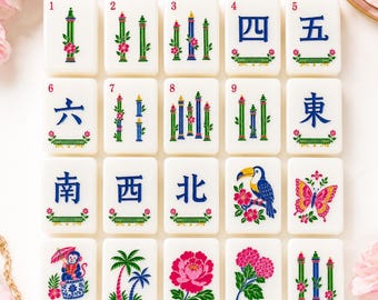 May include: A collection of twenty rectangular white mahjong tiles arranged in a grid. The tiles feature colorful illustrations of bamboo, flowers, a toucan, a butterfly, a monkey with an umbrella, palm trees, and blue Chinese characters.