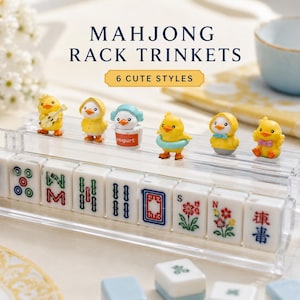Op de afbeelding: Een doorzichtige acryl mahjong-rek met zes kleine gele kuikenfiguurtjes in diverse outfits en accessoires, waaronder een gitaar, regenjas, yoghurtbeker, zwemband en vlinderdas, geplaatst boven een rij witte mahjongstenen met kleurrijke symbolen.