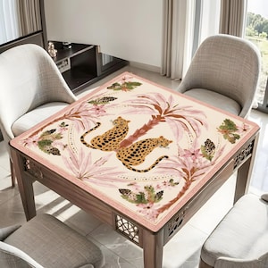 May include: Square wooden table with a cream-colored top featuring a leopard print design. The design includes two leopards, palm trees, and floral elements in shades of pink, brown, and green. The table has decorative cutouts on the sides.