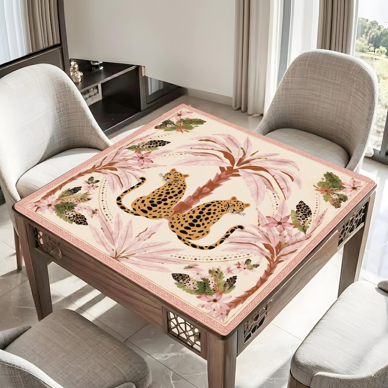May include: Square wooden table with a cream-colored top featuring a leopard print design. The design includes two leopards, palm trees, and floral elements in shades of pink, brown, and green. The table has decorative cutouts on the sides.