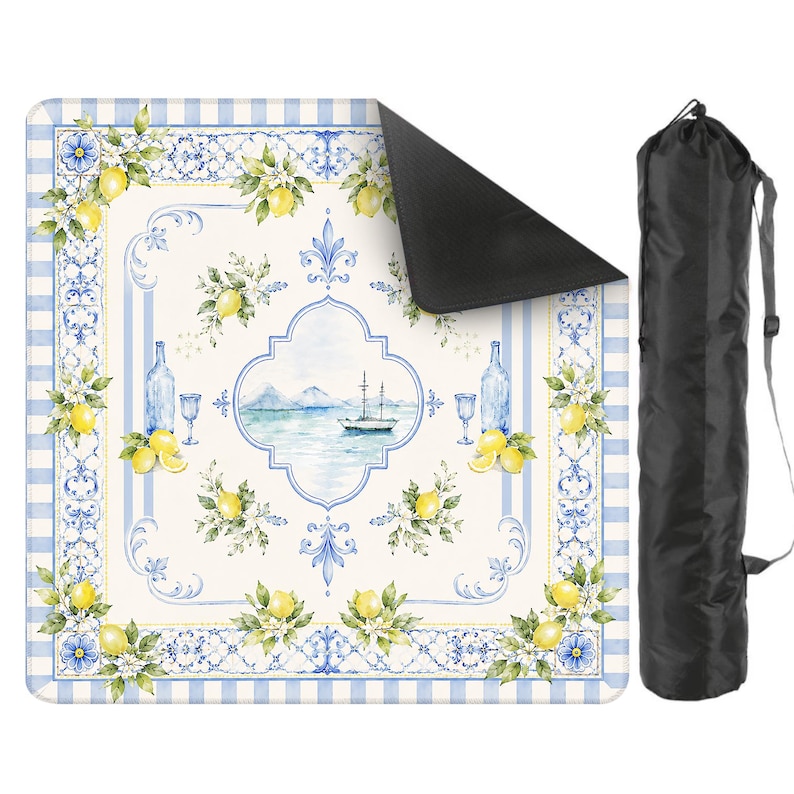 Peut inclure: Une couverture de pique-nique avec une bordure &agrave; carreaux bleus et blancs et un motif central repr&eacute;sentant des citrons, des fleurs et une sc&egrave;ne c&ocirc;ti&egrave;re. La couverture est enroul&eacute;e et rang&eacute;e dans un sac de transport noir avec une bandouli&egrave;re.