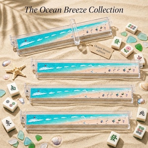Op de afbeelding: De Ocean Breeze Collection. Transparante acryl mahjong-tegelhouders met een strandscène-ontwerp. De rechthoekige houders bevatten een blauwe oceaan en een zandstrand. Mahjong-tegels en strandaccessoires zijn rond de houders verspreid.