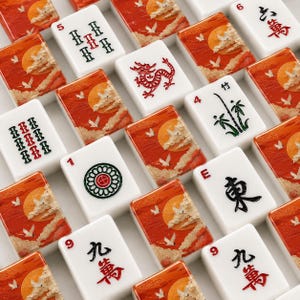May include: A collection of white Mahjong tiles with red, green, and black symbols and numbers. Some tiles feature a sunset design with birds. The tiles are arranged in a grid pattern, showcasing the variety of designs.