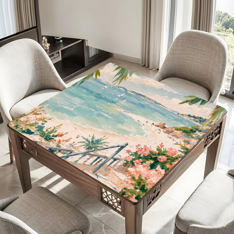May include: A square wooden table with a beach scene painted on the top. The artwork depicts a sandy beach, blue ocean, and palm trees. The table has decorative cutouts on the sides and is surrounded by neutral-colored chairs.