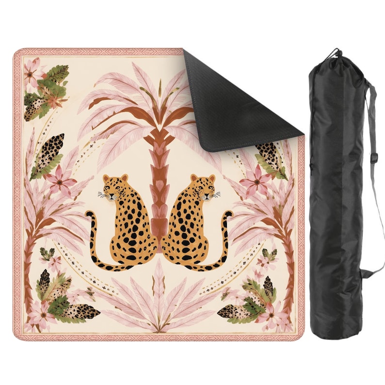 May include: A beige yoga mat with a leopard and palm tree design. The mat features two leopards with black spots, pink palm trees, and floral accents. A black carrying bag is included. The mat has a decorative border.
