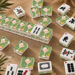 May include: A collection of decorative Mahjong tiles. The tiles feature a green background with a pink cocktail design and olives. Some tiles have black symbols and numbers. The tiles are arranged on a light brown surface.