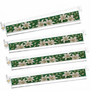Pu&ograve; includere: Quattro telai per cartelle sospese in plastica trasparente, ciascuno dotato di un inserto decorativo con un motivo ripetuto di fiori di giglio bianchi e foglie verdi su sfondo verde scuro, con piccole chiusure metalliche dorate sul lato sinistro.