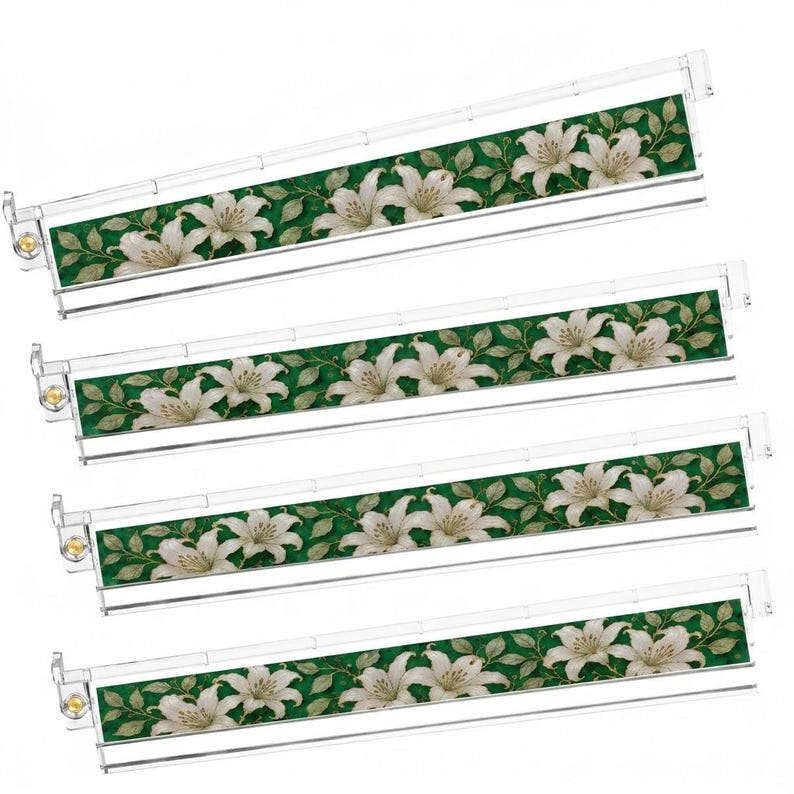 Pu&ograve; includere: Quattro telai per cartelle sospese in plastica trasparente, ciascuno dotato di un inserto decorativo con un motivo ripetuto di fiori di giglio bianchi e foglie verdi su sfondo verde scuro, con piccole chiusure metalliche dorate sul lato sinistro.