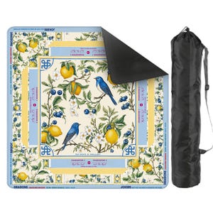 Puede incluir: Una alfombrilla cuadrada con un dise&ntilde;o bot&aacute;nico con limones, ar&aacute;ndanos y p&aacute;jaros azules. La alfombrilla tiene un borde azul claro con texto y va acompa&ntilde;ada de una bolsa de transporte negra. La alfombrilla est&aacute; dise&ntilde;ada para un juego de cartas.