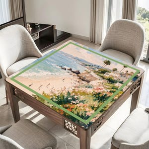 May include: A square wooden table with a painted beach scene on the tabletop. The artwork features a sandy beach, ocean waves, and palm trees, framed by a green border. The table has decorative carved details on the legs.
