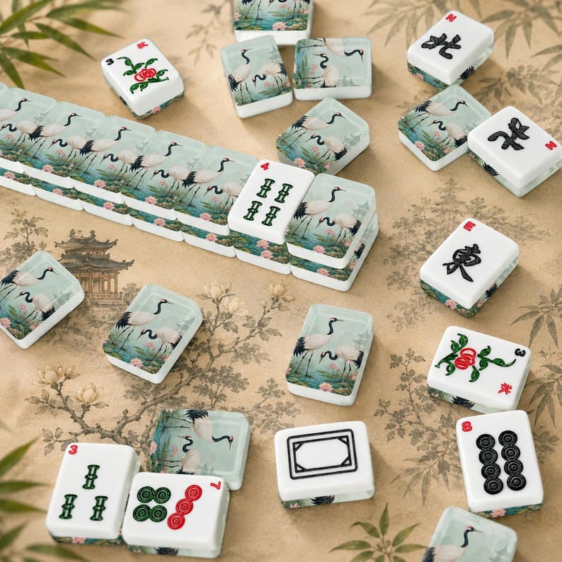 Może przedstawiać: Zbi&oacute;r białych i zielonych płytek do gry w Mahjong z r&oacute;żnymi symbolami i ilustracjami. Niekt&oacute;re płytki przedstawiają żurawie w spokojnym krajobrazie, inne chińskie znaki i wartości liczbowe. Płytki ułożone są na powierzchni z kwiatowym wzorem.