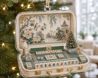 May include: A decorative ornament shaped like an open suitcase containing a miniature mahjong set. The interior features a detailed landscape illustration, a small lamp, a tiny Christmas tree, and various mahjong tiles with Chinese characters.