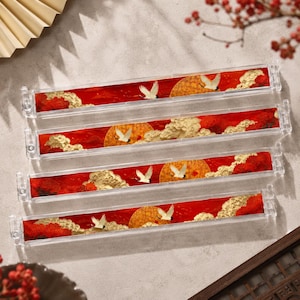 May include: Four clear rectangular containers with a Japanese-inspired design. Each features a red background with a golden sun, white cranes, and clouds. The containers are arranged in a neat stack.