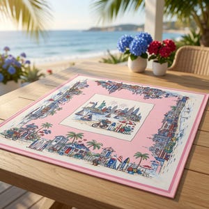 May include: A square fabric placemat with a pink border featuring a detailed illustration of a coastal city skyline, the Statue of Liberty, sailboats, surfboards, palm trees, and beach houses. The central panel depicts a harbor scene.