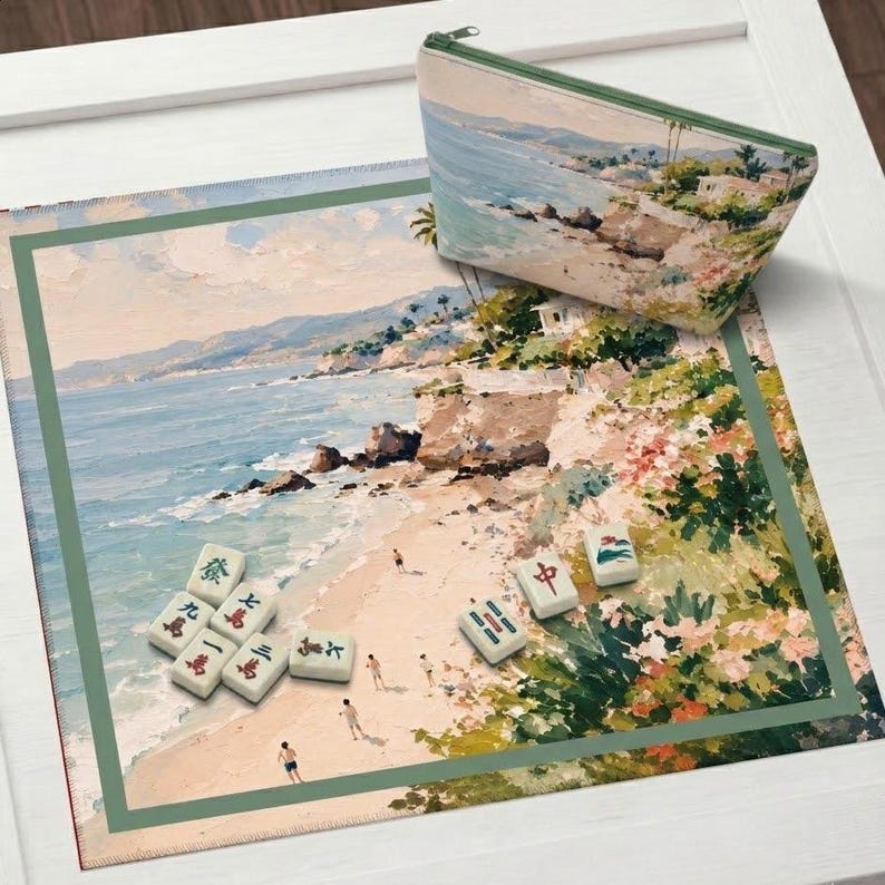 May include: A beach-themed Mahjong set with a matching zippered pouch. The set includes a rectangular mat with a coastal landscape painting and several Mahjong tiles. The pouch and mat feature a similar beach scene with a green border.
