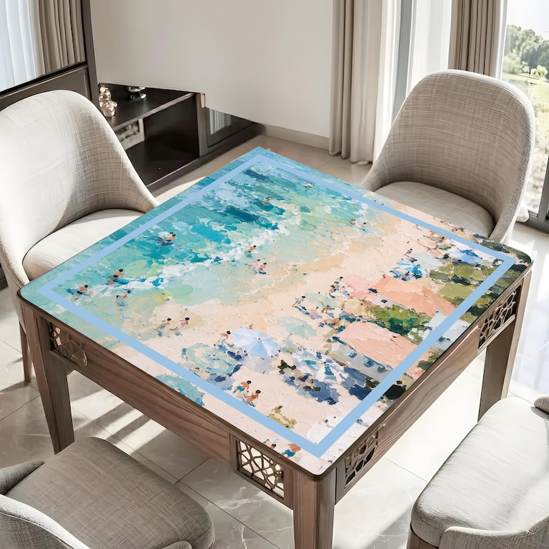 May include: A square wooden table featuring a beach scene painted on its surface. The artwork shows turquoise water, sandy shores, and people. The table has a light blue border. The table is surrounded by chairs.