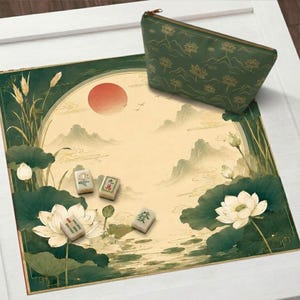 May include: A square mahjong mat featuring a cream-colored center with a red sun and mountain landscape, surrounded by green lotus flowers and reeds. Three mahjong tiles are placed on the mat, accompanied by a matching green zippered pouch.
