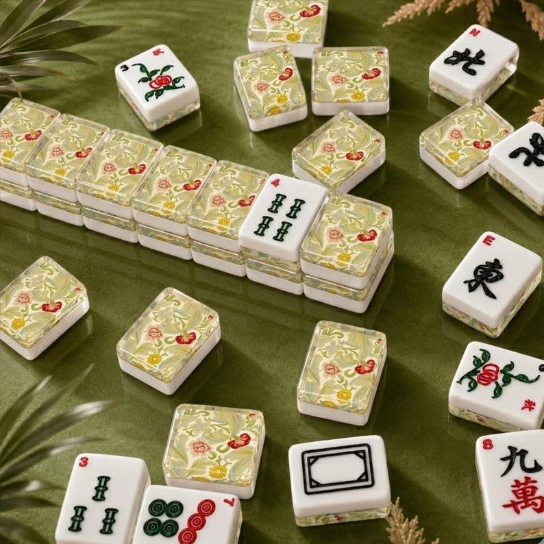 May include: A set of rectangular mahjong tiles featuring a white base with black Chinese characters or red and green floral motifs. Some tiles display a decorative pattern of yellow, red, and green flowers on the back, arranged in a scattered layout.