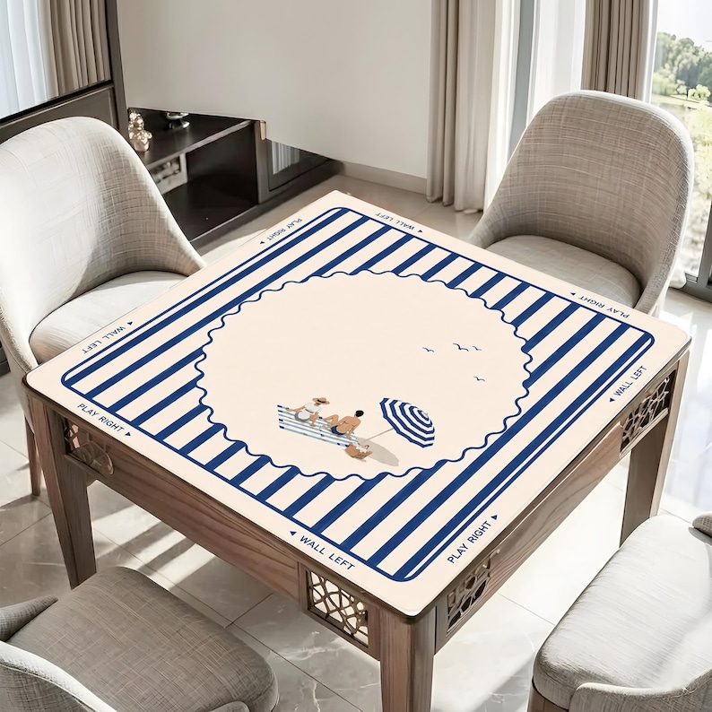 May include: A square wooden table with a beach-themed design. The tabletop features a cream-colored center with a blue striped border and illustrations of people, an umbrella, and birds. The table is surrounded by chairs.