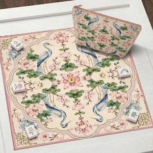 May include: A decorative set featuring a floral and bird design. The set includes a patterned mat, a matching zippered pouch, and several Mahjong tiles. The design features blue herons, pink flowers, and green leaves on a cream background.