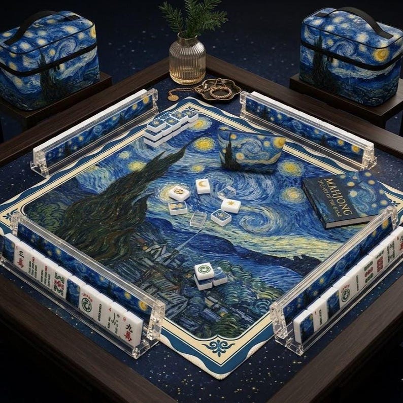 May include: A Mahjong game set featuring a Starry Night art print on the playing mat, four clear acrylic tile racks, a matching storage pouch, two carrying cases, and a book titled Mahjong The Art of the Game, all displayed on a dark table.