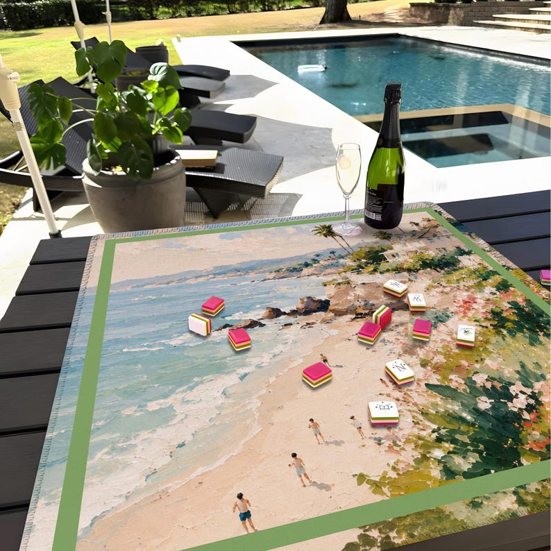 May include: A beach-themed game board with colorful game pieces scattered across a painted beach scene. A bottle of champagne and a glass sit nearby. The scene is set outdoors with a pool in the background.
