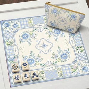May include: A floral-patterned Mahjong set with a matching cosmetic bag. The set features a cream-colored mat with blue floral and plaid designs, and the bag has a gold zipper. Several Mahjong tiles are visible.