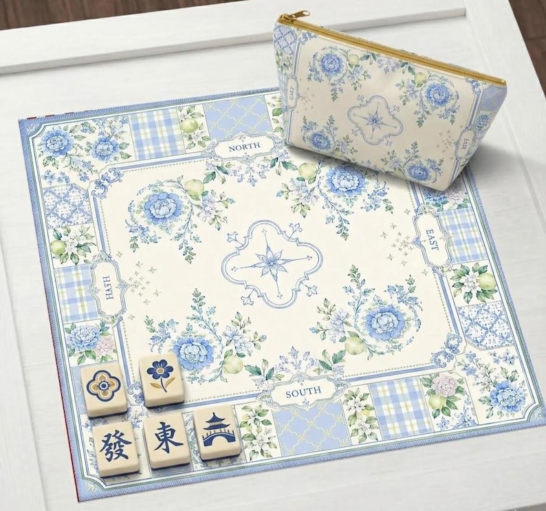 May include: A floral-patterned Mahjong set with a matching cosmetic bag. The set features a cream-colored mat with blue floral and plaid designs, and the bag has a gold zipper. Several Mahjong tiles are visible.