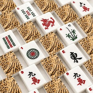May include: A collection of mahjong tiles arranged in a grid pattern. Each tile features a white face with various red, green, and black symbols, numbers, or characters, paired with a textured brown and black leopard print pattern on the back.