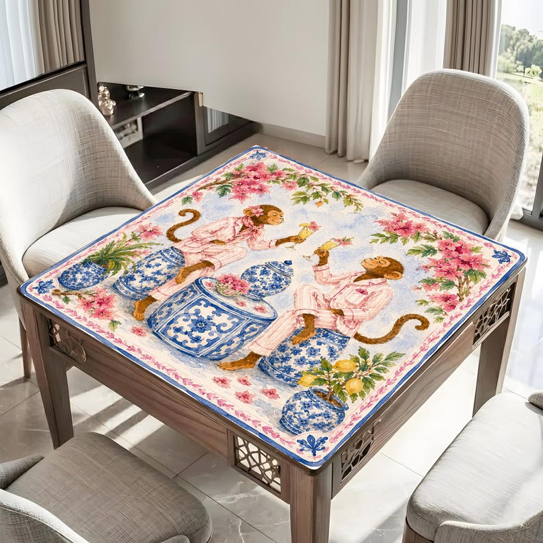 May include: Square wooden table with a decorative cloth featuring a whimsical design. The cloth displays monkeys in pink pajamas, blue and white vases, and pink floral accents. The table is surrounded by chairs.