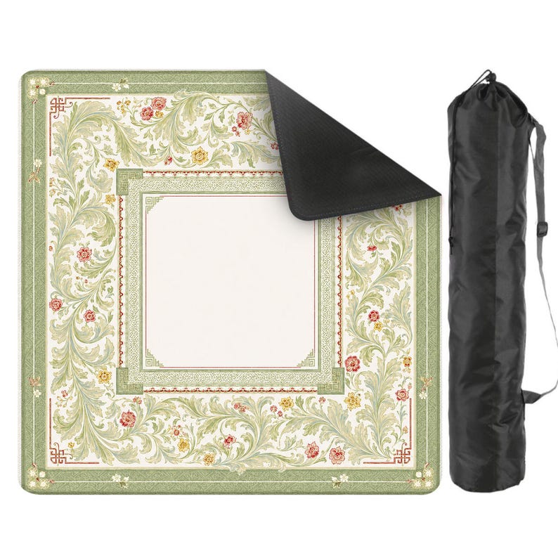 May include: A square picnic blanket featuring a light green border with intricate scrolling foliage and small red and yellow floral accents surrounding a plain cream center. The blanket has a black underside and comes with a black carrying bag.