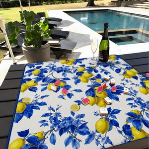 May include: A rectangular, white tablecloth with a blue and yellow lemon and floral pattern. A bottle of champagne and a champagne flute are on the table. Several small, pink and white candies are scattered on the tablecloth.