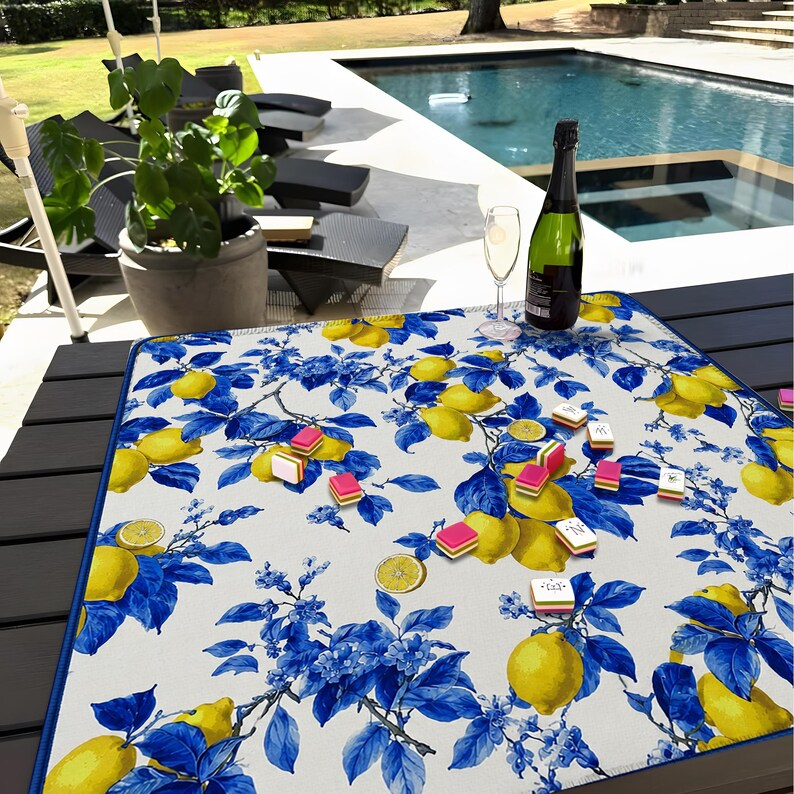 May include: A rectangular, white tablecloth with a blue and yellow lemon and floral pattern. A bottle of champagne and a champagne flute are on the table. Several small, pink and white candies are scattered on the tablecloth.