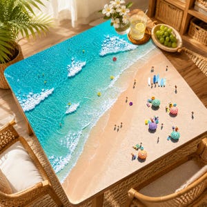 May include: A rectangular table featuring a high-resolution aerial print of a tropical beach scene. The surface displays turquoise ocean water with white foam waves, a sandy shore, and miniature figures of people, surfboards, and umbrellas.