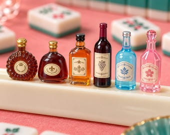 Puede incluir: Un conjunto de seis botellas decorativas en miniatura de diversas formas y colores, incluyendo vidrio ámbar, rojo oscuro y transparente con tonos azules y rosas. Cada botella presenta una etiqueta única con diseños gráficos de uvas y flores.