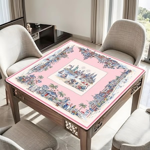 May include: A square tablecloth featuring a central illustration of a coastal city skyline with the Statue of Liberty, surrounded by a pink border decorated with detailed scenes of beach houses, palm trees, surfboards, and bicycles.
