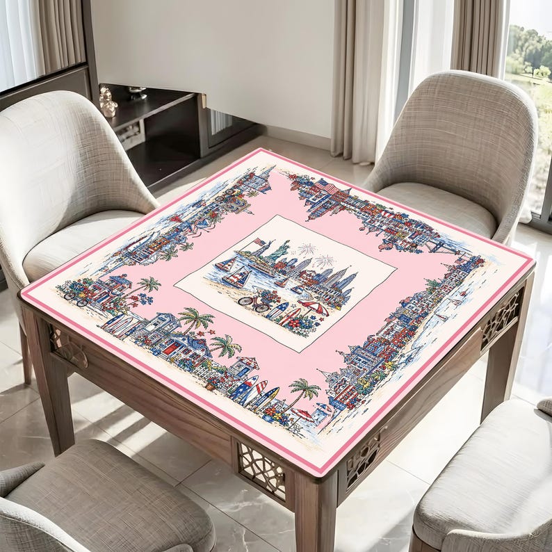May include: A square tablecloth featuring a central illustration of a coastal city skyline with the Statue of Liberty, surrounded by a pink border decorated with detailed scenes of beach houses, palm trees, surfboards, and bicycles.