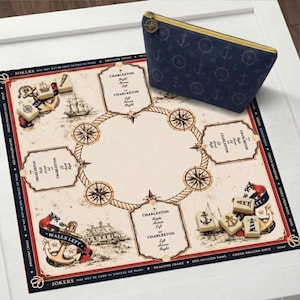 May include: A square game board with a nautical theme featuring compass roses, ships, and lighthouses, alongside a navy blue zippered pouch with a white anchor pattern and a gold-toned compass charm. Several small rectangular game tiles are scattered.