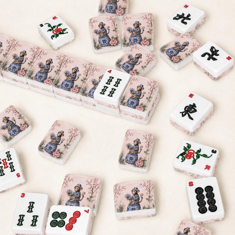Op de afbeelding: Een verzameling witte Mahjong-tegels met roze bloemen- en apenontwerpen. Sommige tegels tonen Chinese karakters en stippen in zwart en rood. De tegels zijn verspreid over een lichtgekleurd oppervlak.