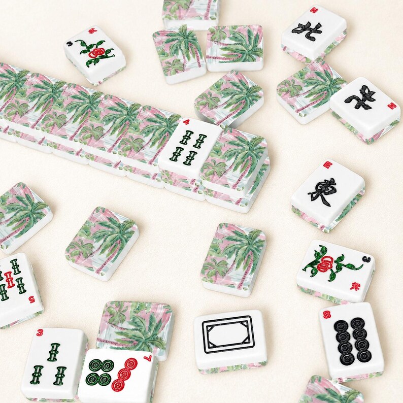 May include: A collection of white Mahjong tiles with various symbols and palm tree designs. Some tiles feature red roses. The tiles are scattered on a light beige surface, creating a visually appealing arrangement.