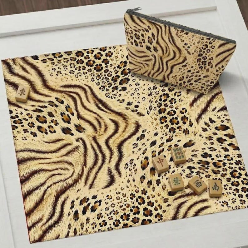 May include: A square mat and a matching zippered pouch featuring a tan, brown, and black animal print pattern. Five small rectangular mahjong tiles with green and black Chinese characters are scattered across the surface of the mat.
