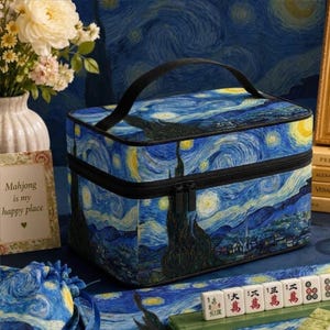 May include: A rectangular storage case featuring a Starry Night print with swirling blue, yellow, and black patterns. The case has a black top handle, a black zipper closure, and a structured design. It is decorated with a classic post-impressionist art style.
