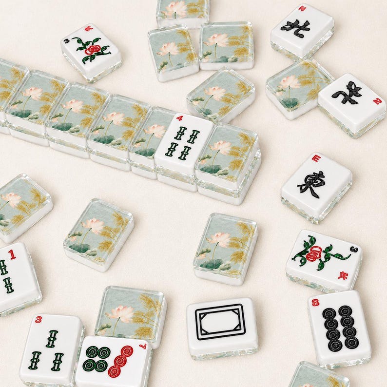 May include: A selection of white and clear Mahjong tiles, each with unique symbols and illustrations. Some tiles showcase floral patterns, while others display numbers and Chinese characters. The tiles are arranged on a light-coloured surface.