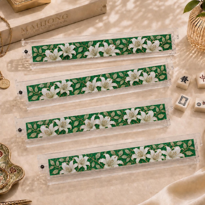 Pu&ograve; includere: Quattro supporti in acrilico trasparente per tessere del mahjong con un inserto decorativo caratterizzato da un motivo ripetuto di fiori di giglio bianchi e foglie verdi su sfondo verde scuro. Ogni supporto ha una piccola vite nera a sinistra.