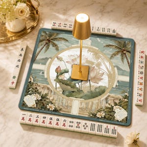 May include: A square mahjong mat featuring a tropical landscape with palm trees and lotus flowers, surrounded by four racks of mahjong tiles with Chinese characters and symbols. A gold-colored metal lamp stands in the center of the mat.