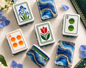 May include: A collection of rectangular mahjong tiles featuring various designs, including blue and gold marbled patterns, a blue iris flower, a red tulip, a green number two with circles, and an orange number four with four circles.